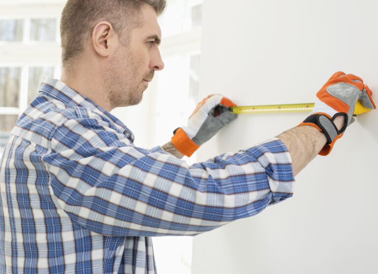 Man measuring wall with woman painting in background